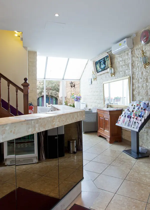 Réception d'un hôtel avec comptoir et brochures, près d'un escalier et d'une fenêtre lumineuse.