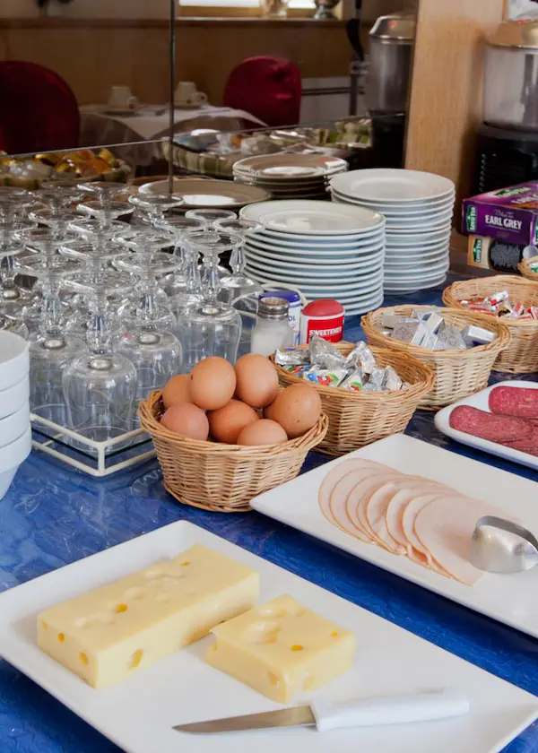 Buffet de petit déjeuner avec fromage, charcuterie, œufs, et vaisselle empilée.