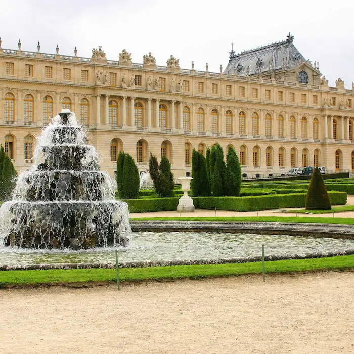 Fontaine devant un grand bâtiment classique entouré de jardins bien entretenus.