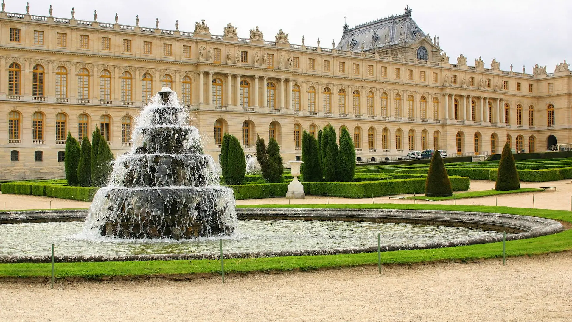 Fontaine du jardin devant le château de Versailles, avec buissons et architecture classique.