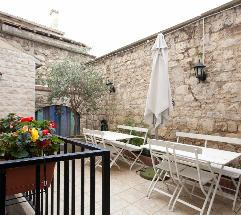 Petite terrasse en pierre avec mobilier blanc, fleurs colorées et parasol fermé.