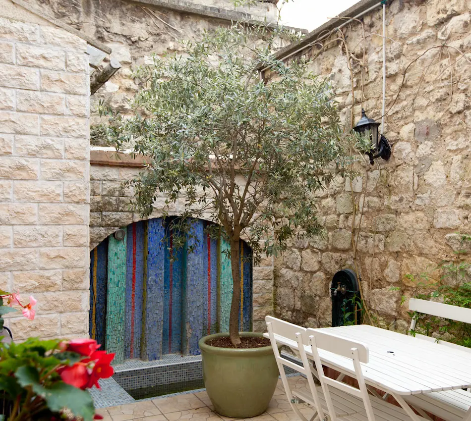 Cour intérieure avec table blanche, arbre en pot et mur en pierre coloré.