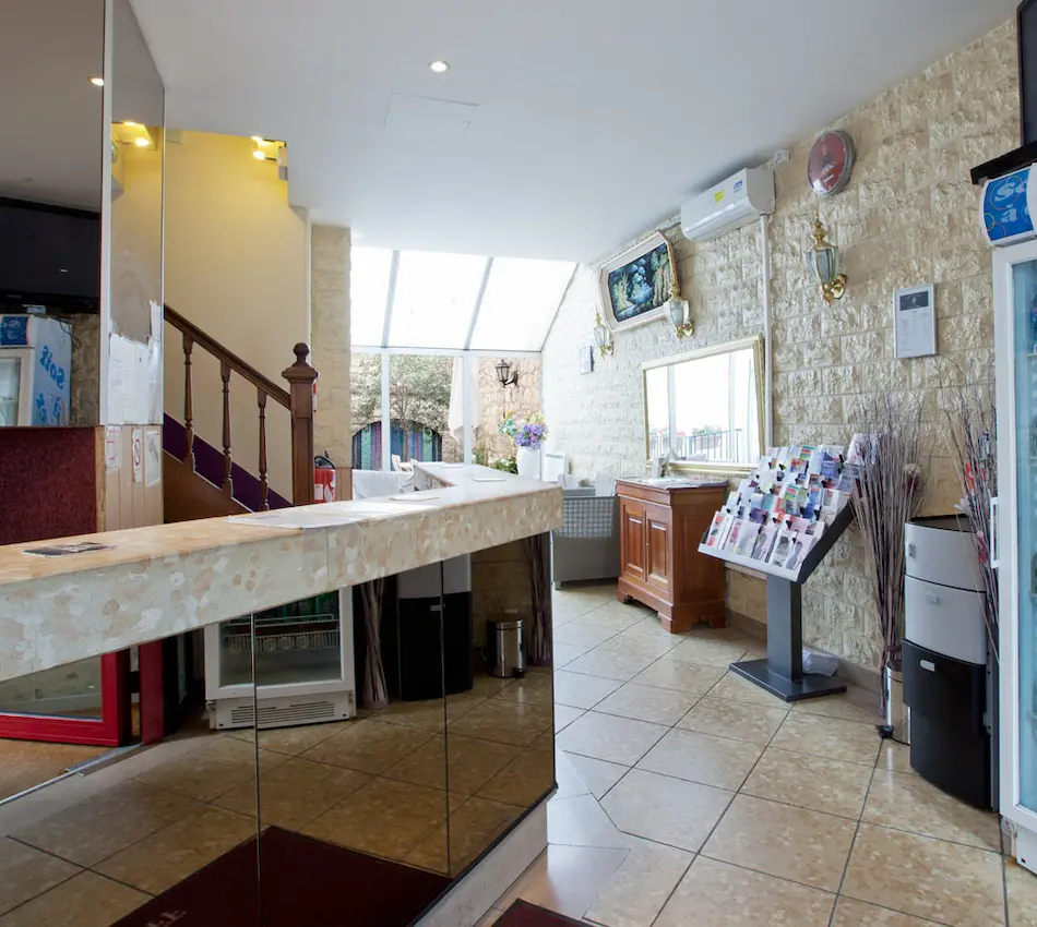Réception d'hôtel lumineuse avec comptoir en pierre, escalier en bois et présentoir de brochures.