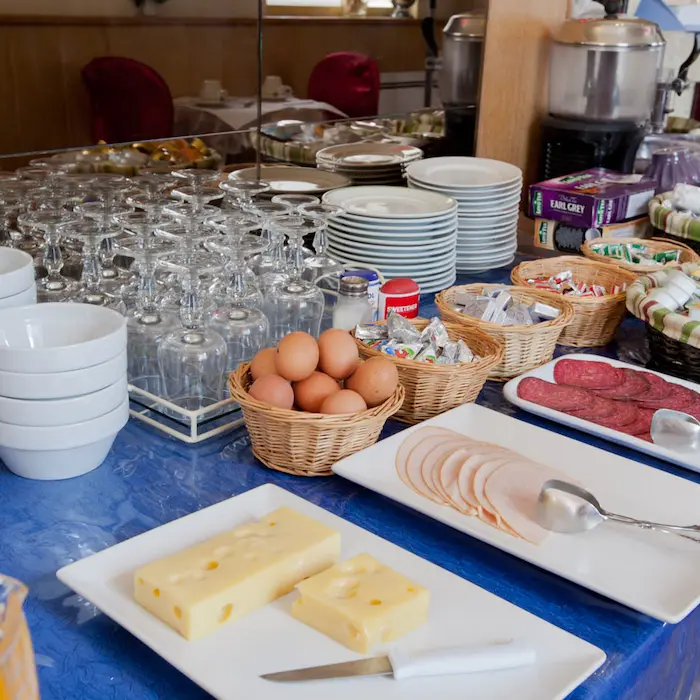 Buffet de petit-déjeuner avec œufs, fromage, charcuterie, assiettes et verres empilés.