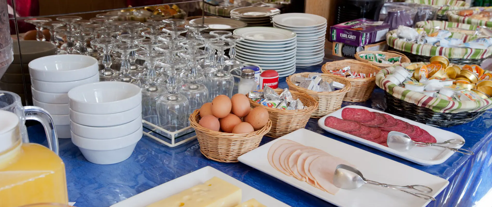 Buffet de petit-déjeuner avec œufs, charcuterie, fromage et boissons.
