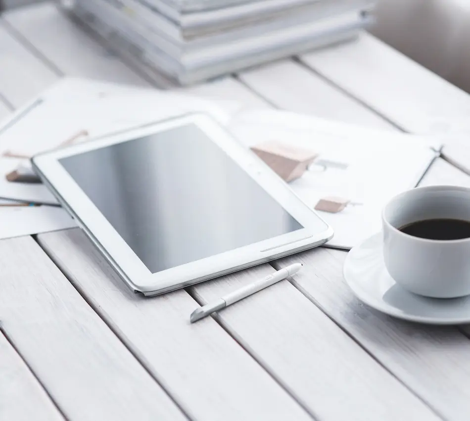 Tablette, stylet et tasse de café sur une table blanche.