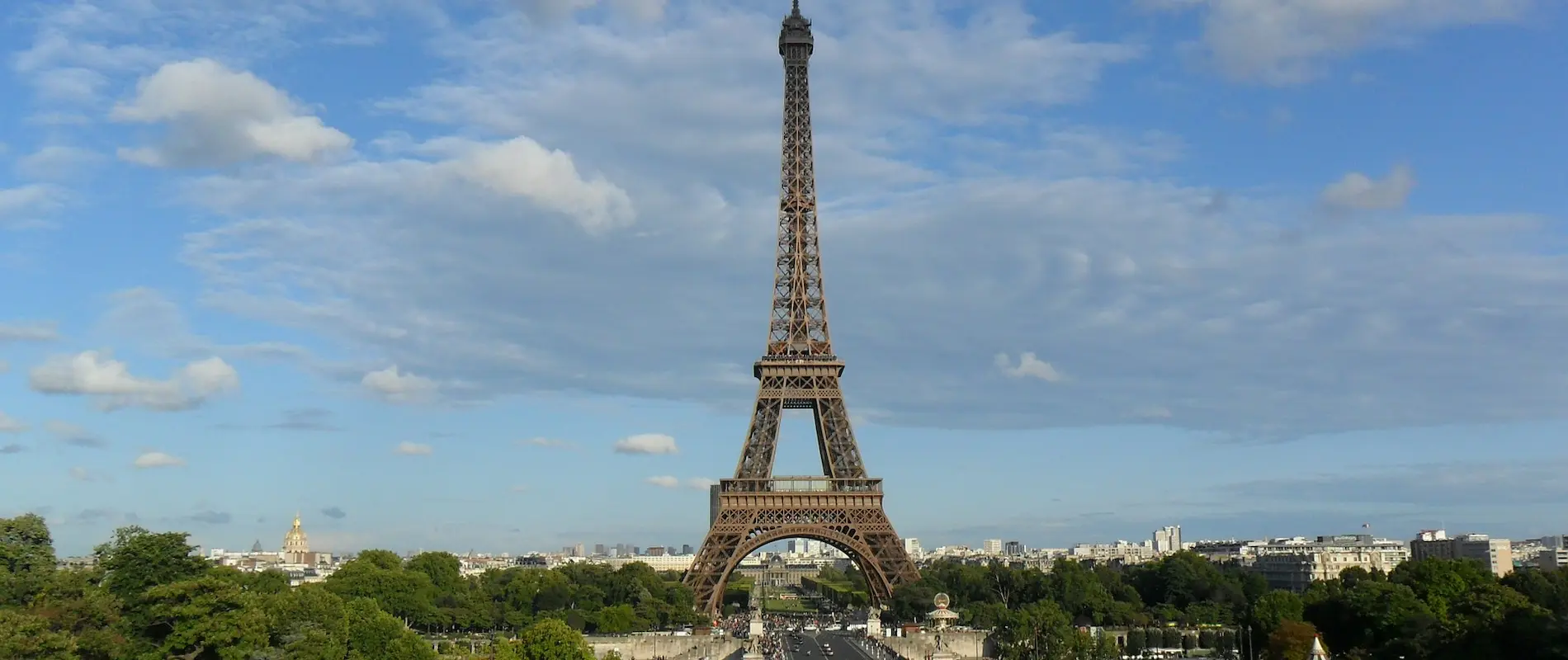 Tour Eiffel sous un ciel bleu avec quelques nuages flottants.