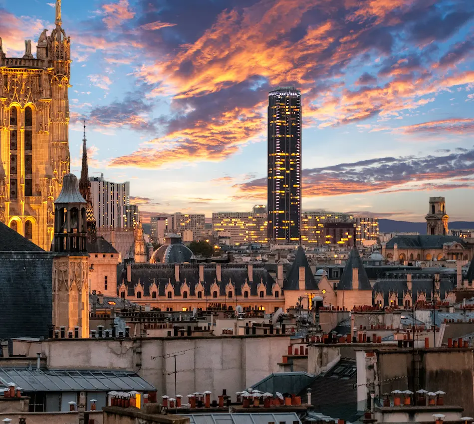 Immeubles au crépuscule avec nuages colorés et tour moderne illuminée en arrière-plan.