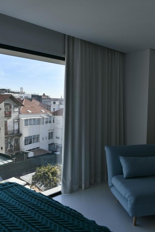Vista de uma janela mostrando edifícios com telhados vermelhos, parte de uma cama e um sofá azul no canto direito.