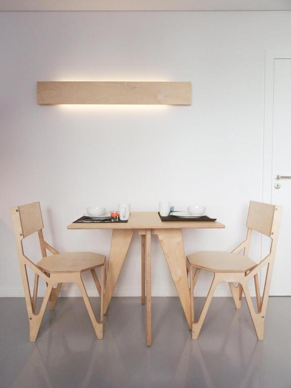 Mesa de madeira para duas pessoas, com louça simples e cadeiras modernas, em ambiente minimalista.