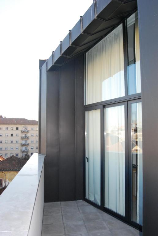 Varanda moderna com porta de vidro, cercada por estrutura metálica escura, vista lateral de prédio residencial.
