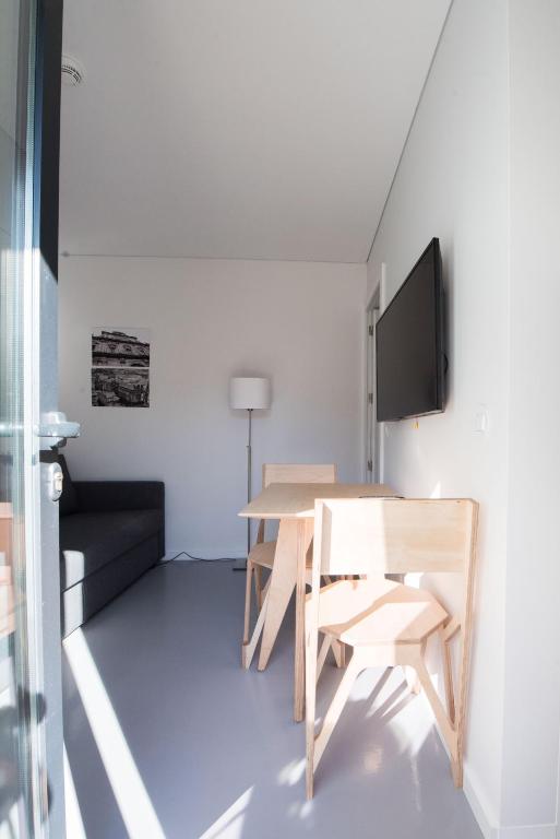 Sala moderna e minimalista com sofá, mesa e cadeiras de madeira, TV na parede e lâmpada de pé branca.
