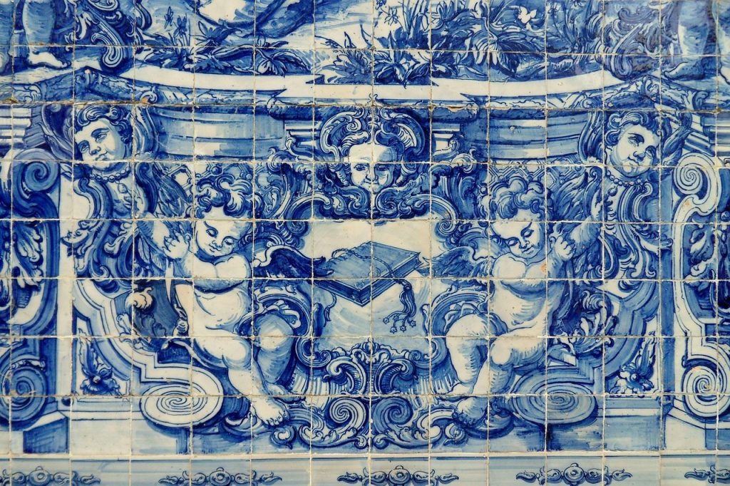 Azulejos azuis com anjos e faces ornamentadas em um estilo barroco, segurando um livro aberto.