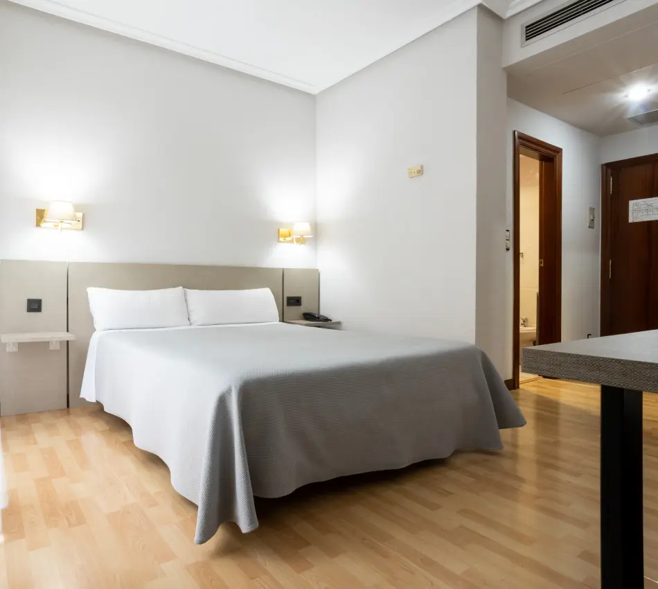 habitaci&oacute;n con cama de matrimonio con colcha gris y suelo de parquet