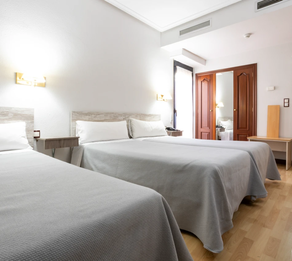 Habitaci&oacute;n de hotel con 3 camas y un armario de madera.