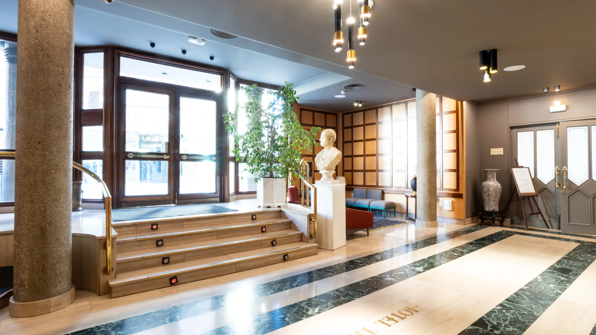 Vest&iacute;bulo elegante con escultura, planta y puertas de vidrio grandes.