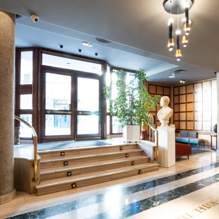 Vest&iacute;bulo elegante con escalera, planta y busto en pedestal.