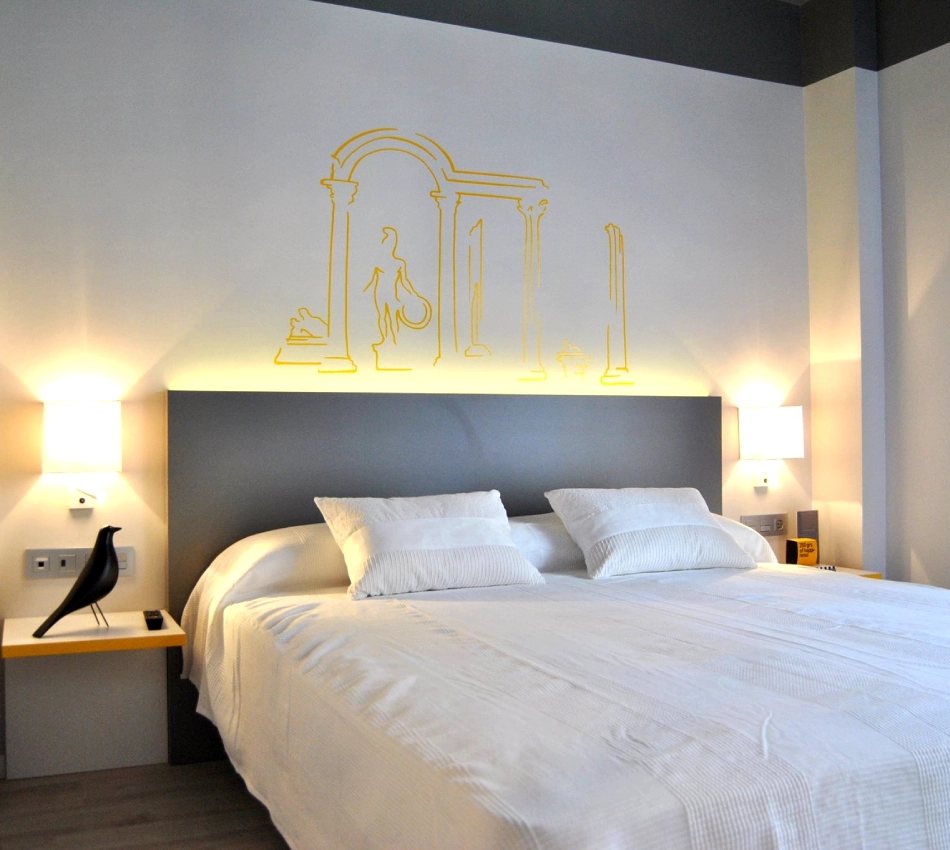 Cama doble con dise&ntilde;o de columnas amarillas en la pared, l&aacute;mparas a ambos lados.