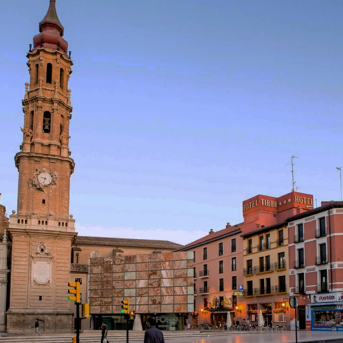 Torre alta con reloj junto a edificios y hotel bajo cielo despejado.