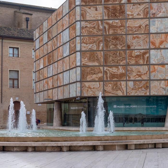 Edificio moderno con fachada de m&aacute;rmol y fuente frente al Museo del Foro de Caesaraugusta.