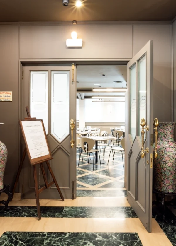 Puerta abierta de restaurante elegante con mesas al fondo.