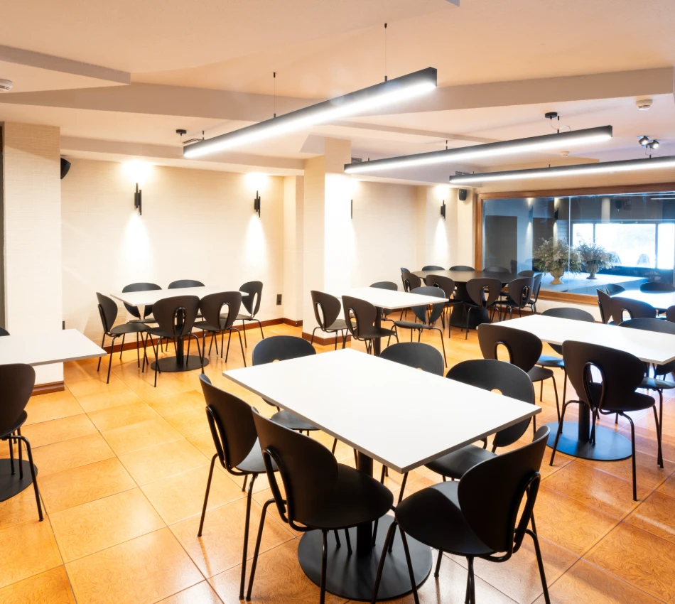 Comedor moderno con mesas blancas y sillas negras, bien iluminado.