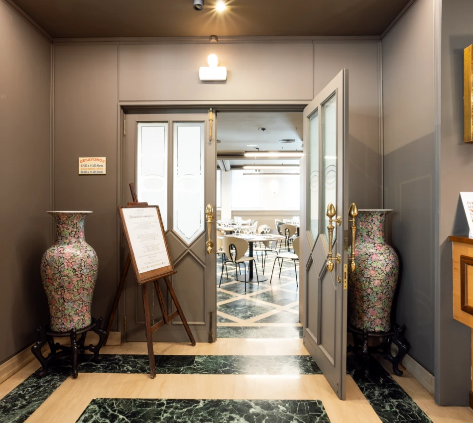 Puertas abiertas hacia un sal&oacute;n de desayunos con jarrones decorativos a los lados.