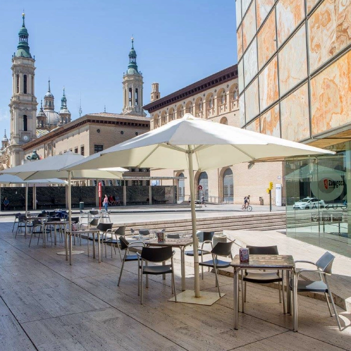 Terraza con sombrillas y sillas, edificios hist&oacute;ricos y personas paseando en bicicleta al fondo.