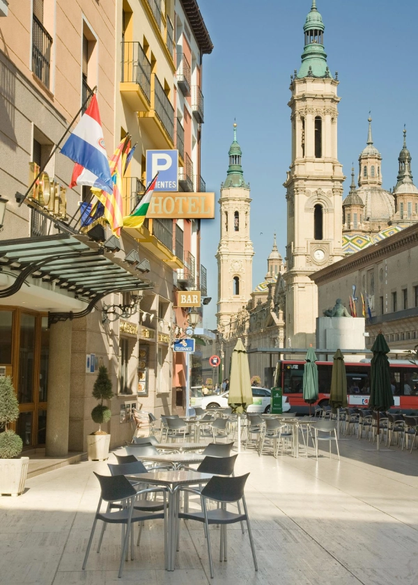 Calle de Zaragoza con sillas de caf&eacute; al aire libre y vistas a edificio hist&oacute;rico con torres.