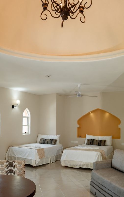 Habitación con dos camas, sofá gris, ventanas y lámpara de techo elegante. Decoración minimalista.