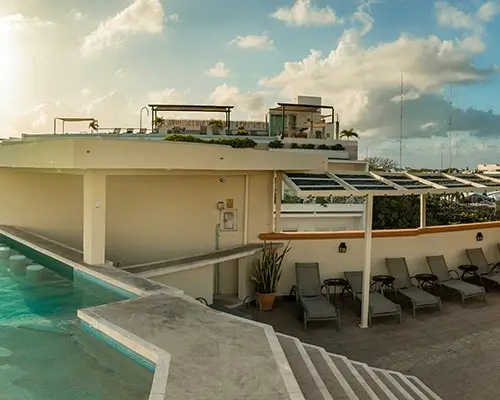 Terraza con piscina, camastros y cielo parcialmente nublado al atardecer.