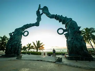 Arco escultórico frente al mar con palmeras al amanecer en Playa del Carmen.
