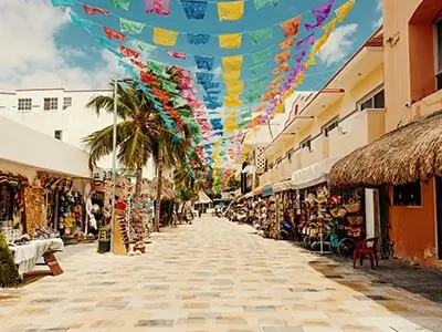 Calle peatonal con banderines de colores, tiendas a los lados y cielo despejado.