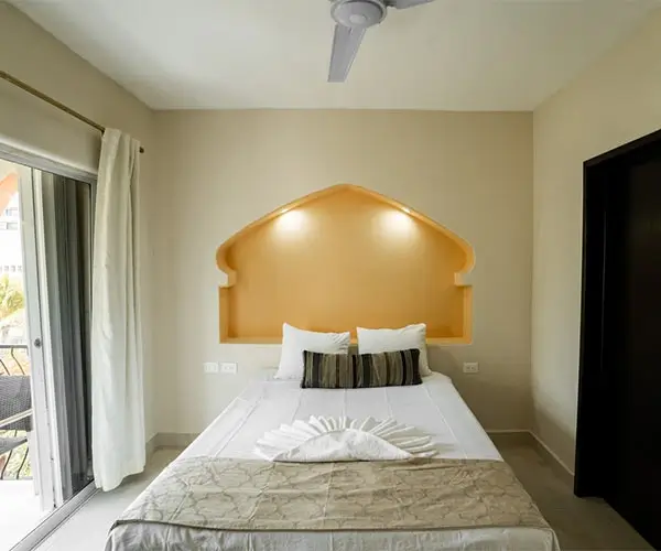 Habitación minimalista con cama, ventanal a la izquierda y lámparas en pared decorativa naranja.