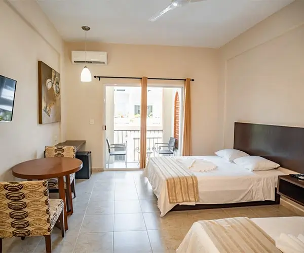 Habitación de hotel luminosa con cama doble, mesa, sillas y balcón con vista exterior.