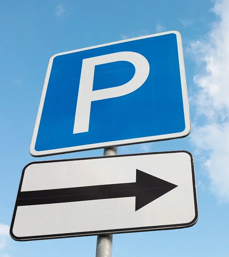 Señal de estacionamiento con flecha negra apuntando a la derecha, fondo de cielo azul.