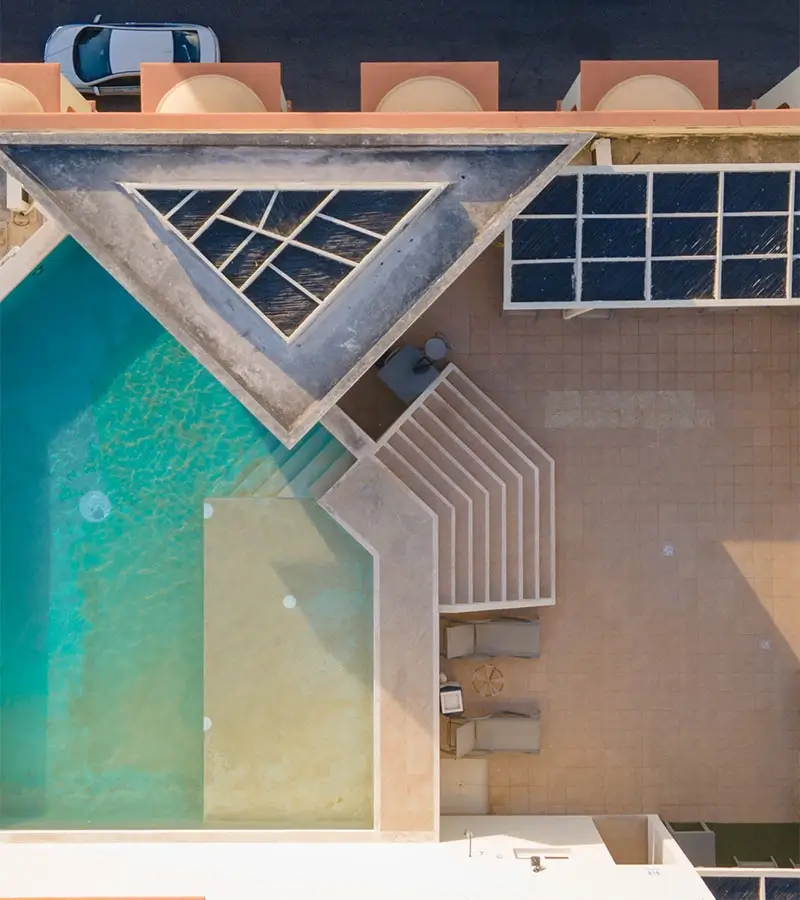 Vista aérea de una piscina y un patio con sillones, diseño geométrico y camino lateral.
