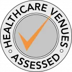 Sello circular gris con un cheque naranja y las palabras "Healthcare Venues Assessed" alrededor.