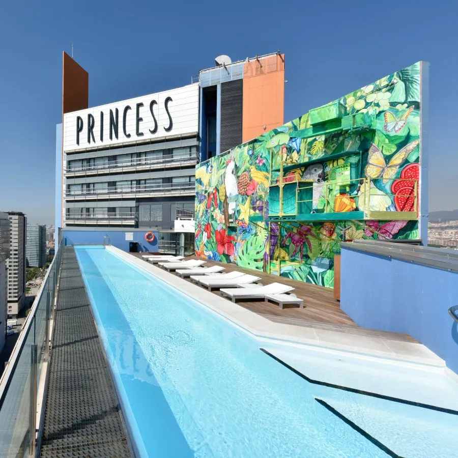 Piscina en la azotea de un edificio moderno, con mural colorido al fondo y tumbonas alineadas.
