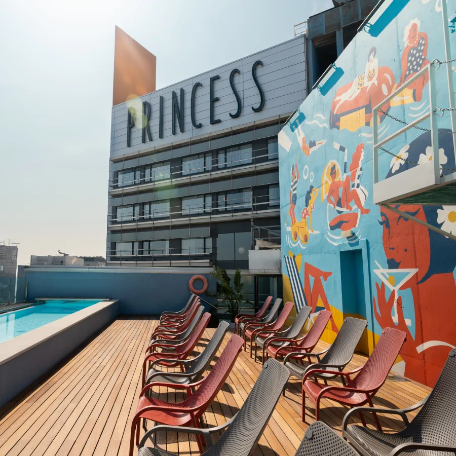 Azotea con sillas junto a piscina, mural colorido y edificio con letrero "Princess".