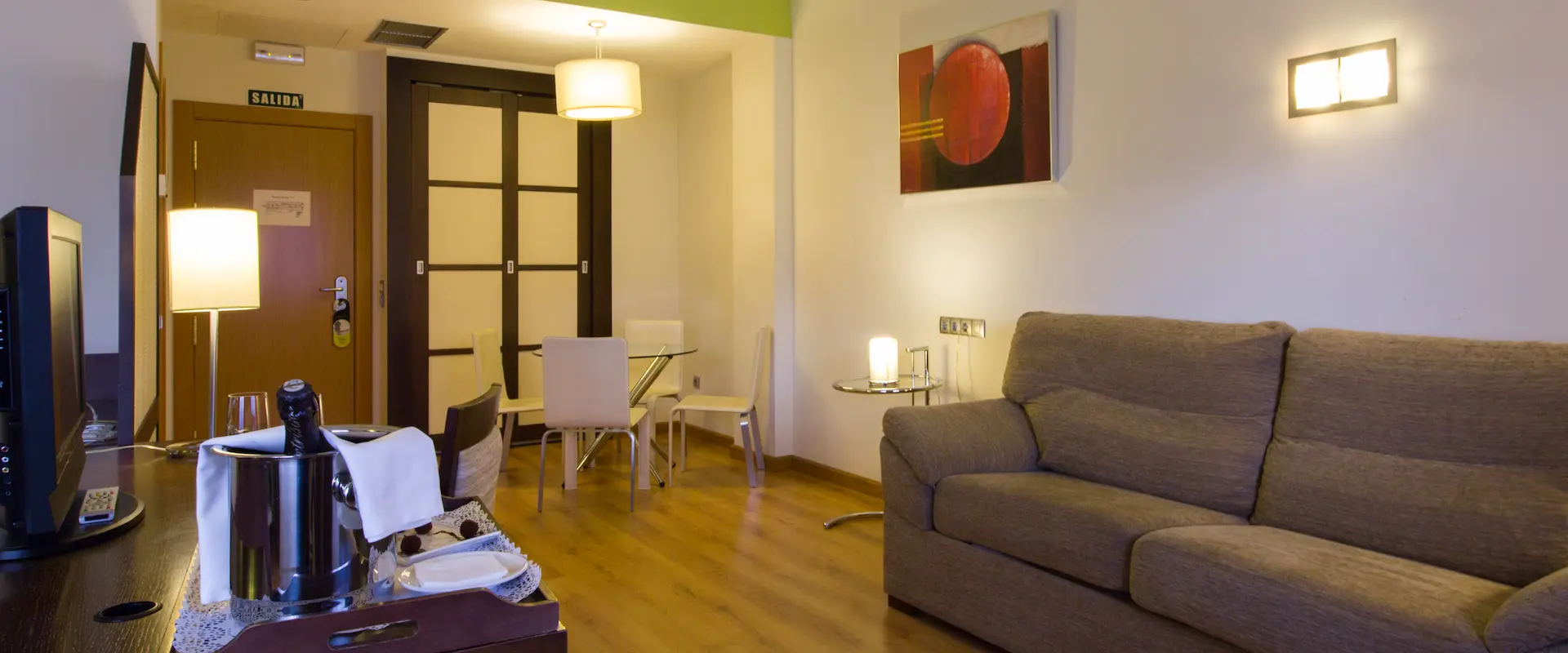 Sala moderna con sofá gris, mesa de vidrio, lámparas y pintura abstracta en la pared.