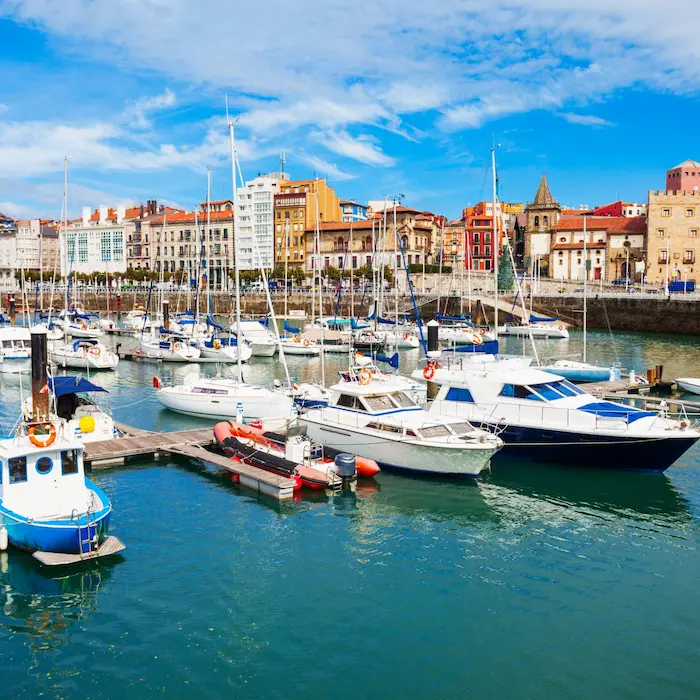 Barcos atracados en un puerto con edificios coloridos al fondo bajo un cielo azul.