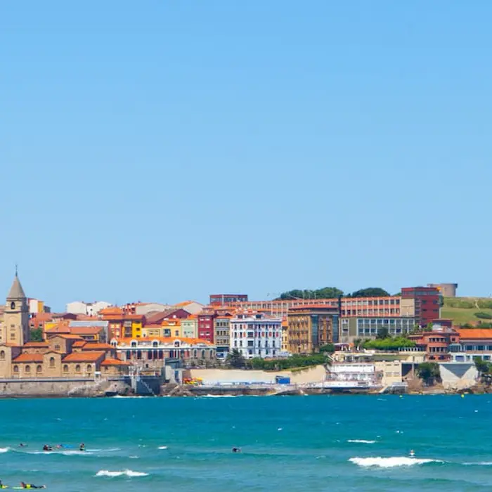Vista de una ciudad costera con edificios coloridos y el mar en primer plano bajo un cielo azul.