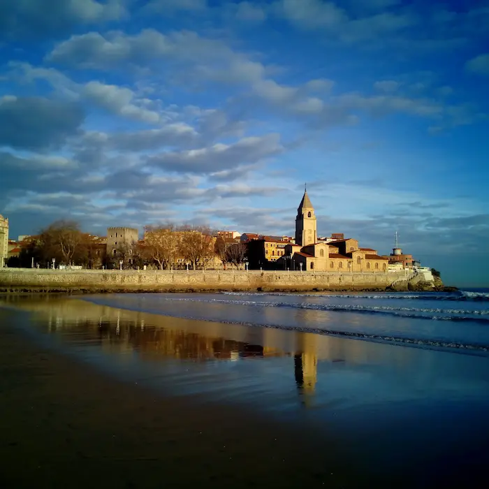 Iglesia al atardecer reflejada en una playa tranquila, con un cielo azul y nubes dispersas.