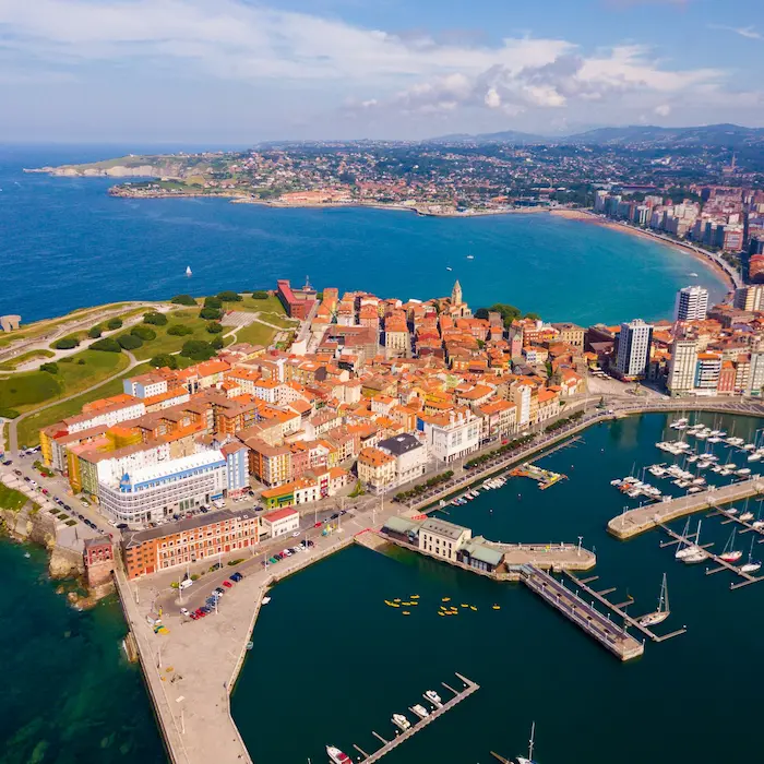 Vista aérea de una ciudad costera con un puerto y edificios coloridos junto al mar azul.