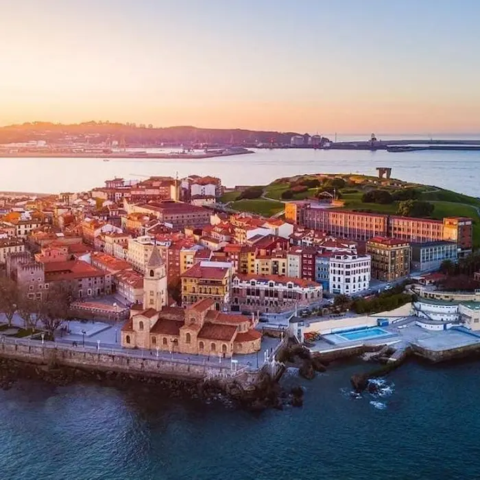 Vista aérea de un pueblo costero con una iglesia y edificios al atardecer, junto al mar.