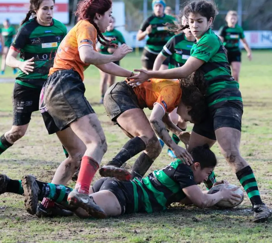 Jugadoras de rugby en acción sobre un campo de juego, luchando por el control del balón.