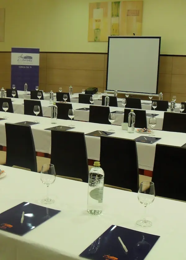 Sala de conferencias con sillas, mesas, cuadernos y botellas de agua dispuestos para un evento.