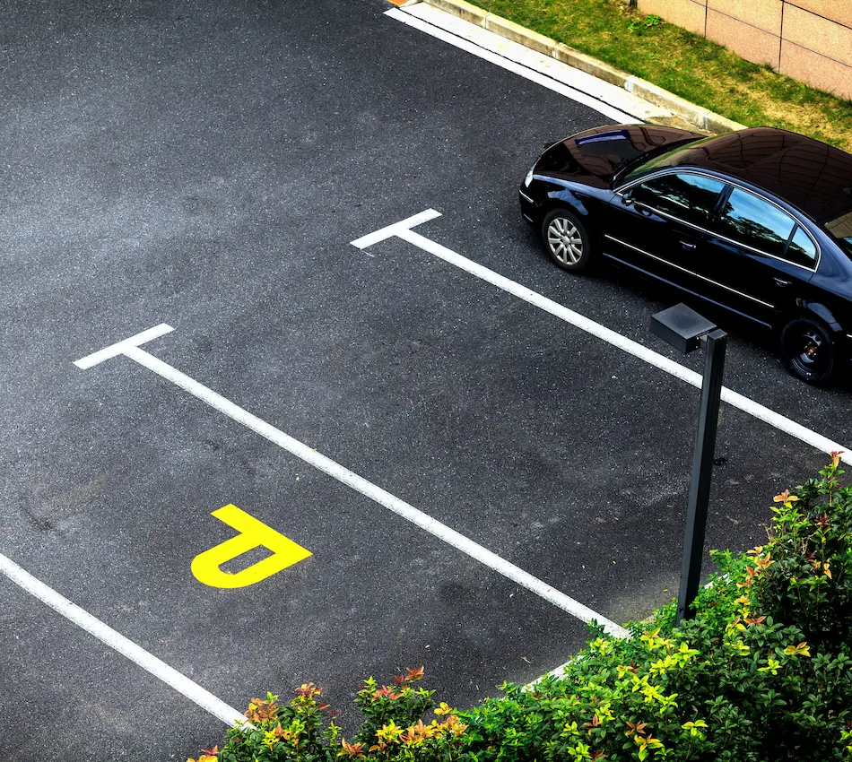 Auto negro estacionado junto a líneas de estacionamiento vacías y un signo amarillo en el suelo.