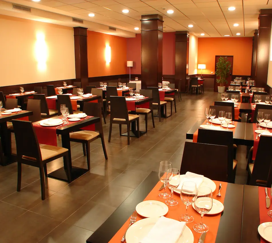 Restaurante elegante con mesas preparadas, sillas de madera y luces cálidas en el techo.